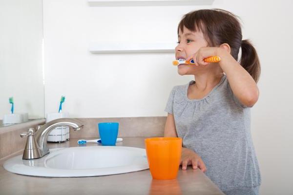 小女孩用橙色的牙刷和杯子刷牙